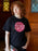 Person wearing a black t-shirt with 'Misery and Company' design, standing indoors.
