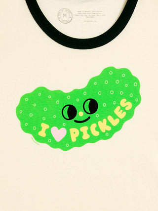 A close-up of a cream-colored ringer t-shirt featuring a bright green pickle-shaped graphic with a cute face and the text 'I [heart] PICKLES' in yellow, with a forest green collar.
