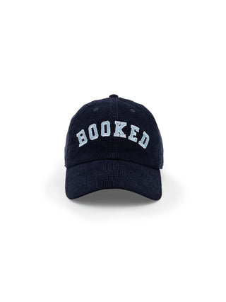 A navy blue corduroy baseball cap with the word 'BOOKED' embroidered in white letters on the front.