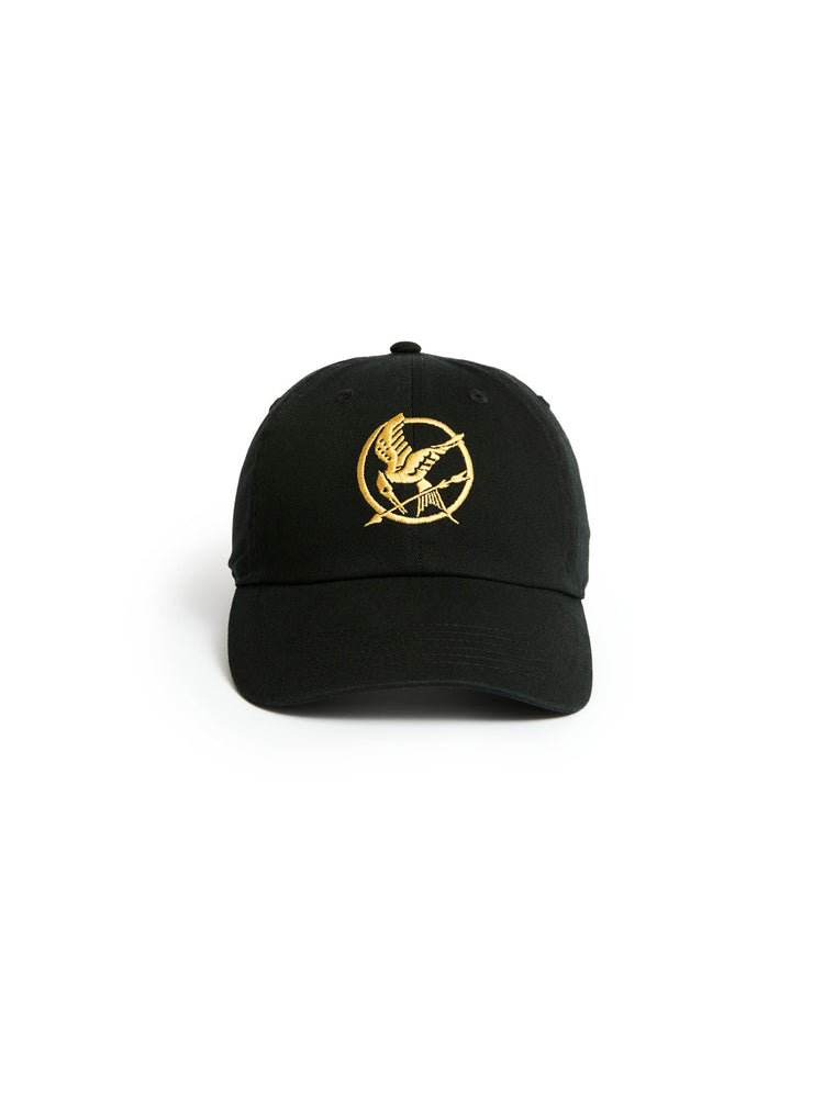 A black baseball cap featuring an embroidered gold Mockingjay logo on the front, set against a plain white background.