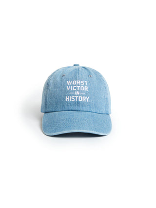 A light blue denim baseball cap with white embroidered text reading 'WORST VICTOR IN HISTORY' on the front, shown against a plain white background.