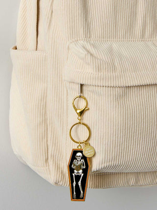 Keychain with skeleton design attached to a beige corduroy bag.