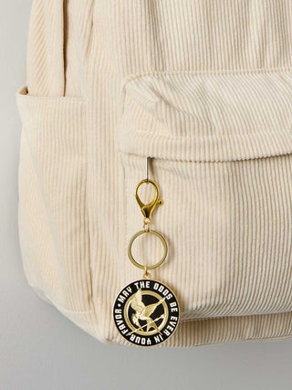 Beige corduroy bag with a keychain featuring a circular emblem on a light gray background