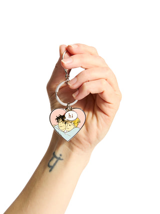 Heart-shaped keychain with cartoon design held by a hand on a white background