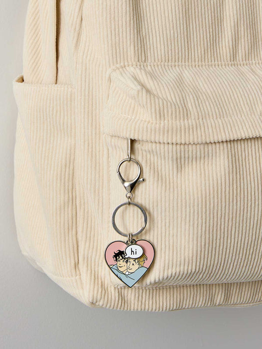 Heart-shaped keychain with cartoon design attached to a beige corduroy bag.