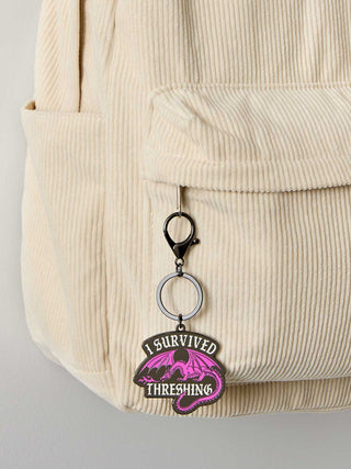 Keychain with 'I Survived Threshing' text attached to a beige corduroy bag.