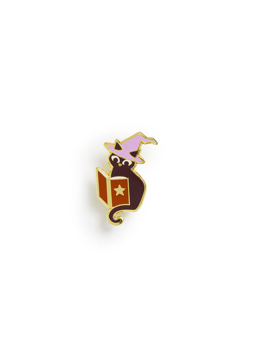 Enamel pin of a black cat wearing a witch hat and reading a spellbook on a white background
