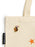 Close-up of a cream canvas tote bag with a small multicolor witch pin on the front, an orange star graphic, and a black 'OUT OF PRINT' brand tag.
