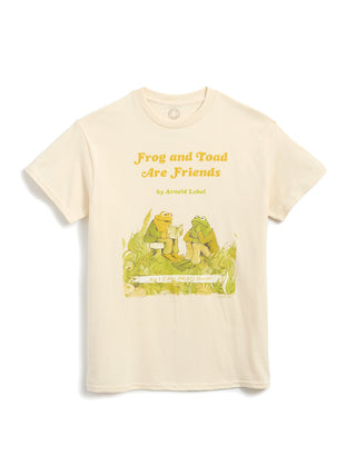 A cream-colored short-sleeve t-shirt featuring a graphic print of a green frog and a yellow-green toad sitting on a log, with the text 'Frog and Toad Are Friends' and 'by Arnold Llobel' printed above them.