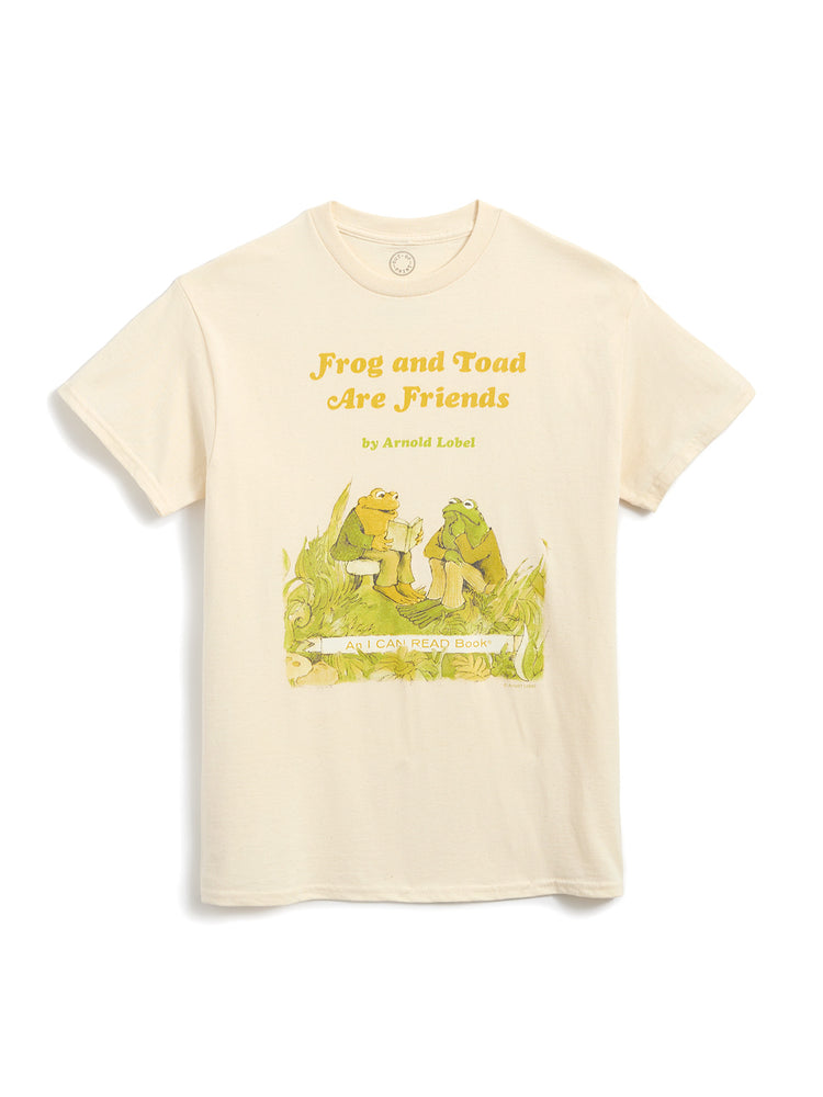 A cream-colored short-sleeve t-shirt featuring a graphic print of a green frog and a yellow-green toad sitting on a log, with the text 'Frog and Toad Are Friends' and 'by Arnold Llobel' printed above them.