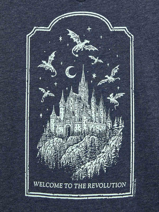 A close-up of a dark navy heathered fabric featuring a white distressed graphic print of a castle, dragons, stars, and a crescent moon, with the text 'WELCOME TO THE REVOLUTION' at the bottom.