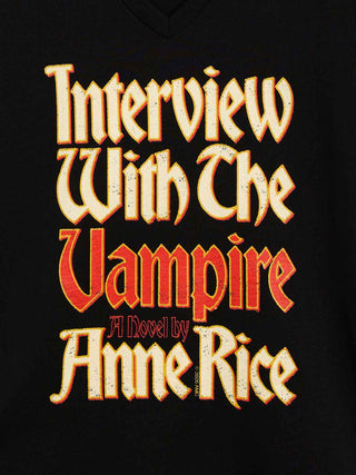 A close-up of a black v-neck t-shirt featuring a large, stylized graphic print of the book cover for 'Interview With The Vampire A Novel by Anne Rice' in a distressed gothic font.