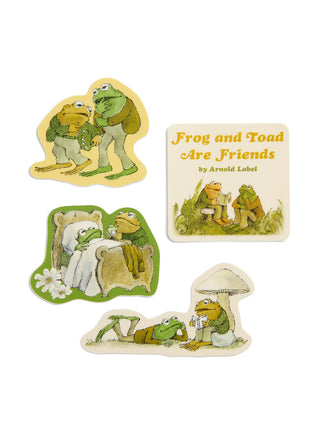 Four illustrated frog-themed items on a plain white background: 2 character stickers, a square book cover reading 'Frog and Toad Are Friends' by Arnold Lobel, and a small rounded patch or badge with a frog and mushroom scene.