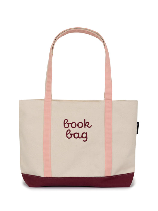 A large zippered tote bag made of canvas with peaches and cream colored straps and burgundy bottom, labeled 'book bag'.