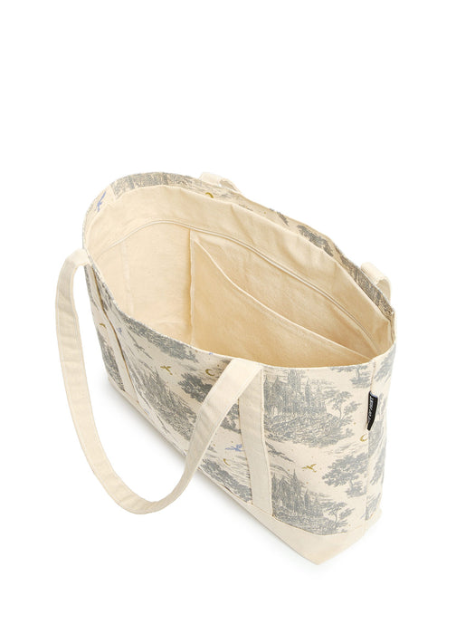 A canvas tote bag with a classic toile de jouy landscape print in beige and gray, featuring cream-colored fabric handles and a cream interior lining.
