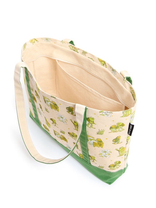 A canvas tote bag with a green frog print on a cream background, featuring a solid green bottom panel and green trim, shown open on a white background.