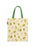 A canvas tote bag with a light beige background printed with a whimsical pattern of green frogs, white flowers, and small yellow dots. The bag has two green fabric handles and a small black brand tag on the left side.