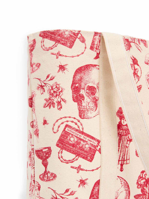 A close-up of a canvas tote bag featuring a red vintage-style graphic print on a cream background, with red shoulder straps visible on the right side.