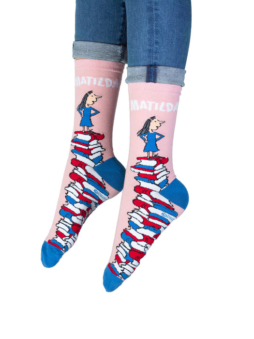A pair of pink socks with an illustration of a character standing on a stack of books, with the name 'Matilda' written across the top.